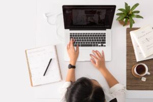 Person sat at desk with laptop, notebook and plant